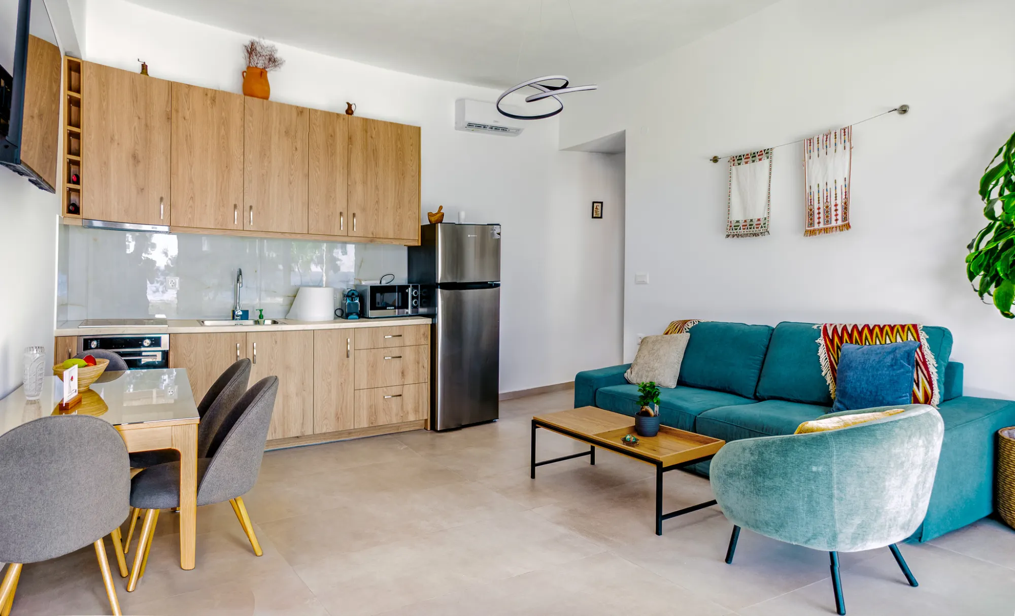 The apartment's open living space — teal sofa, oak kitchen along the wall, dining table by the window