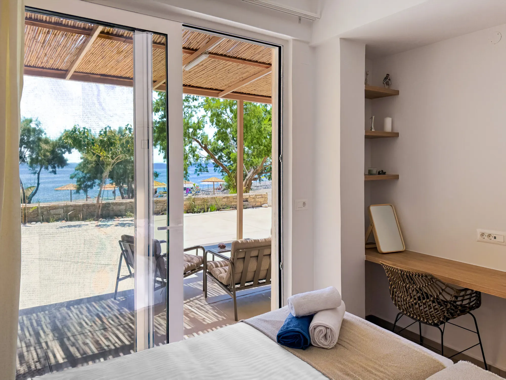 From the bed, through open glass doors — the bamboo pergola, the terrace, the tamarisk trees and the sea