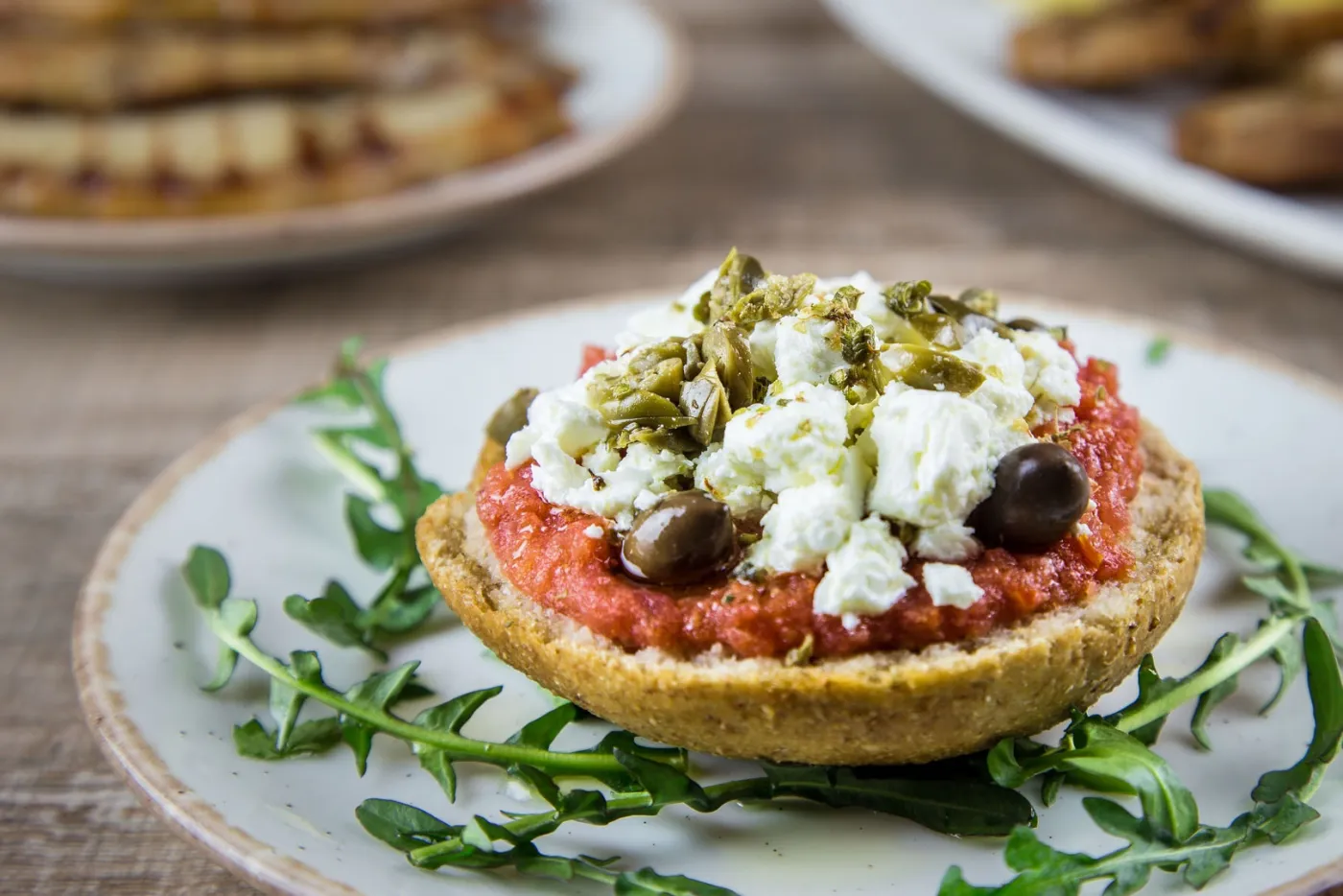 Cretan dakos — a barley rusk topped with grated tomato, crumbled mizithra cheese, capers and olives on rocket