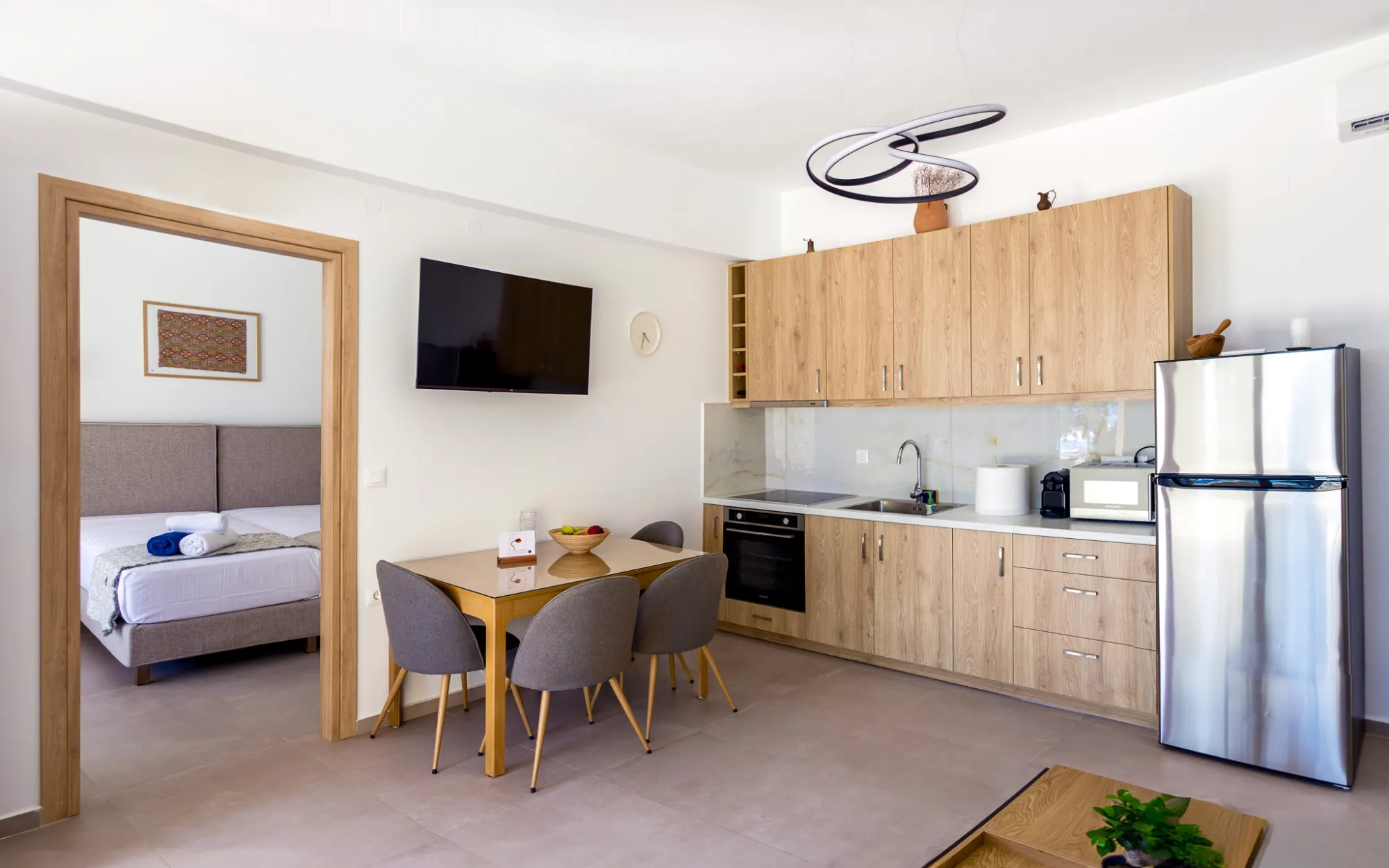 The apartment's open living space with the dining table, TV and oak kitchen — one bedroom visible through its doorway