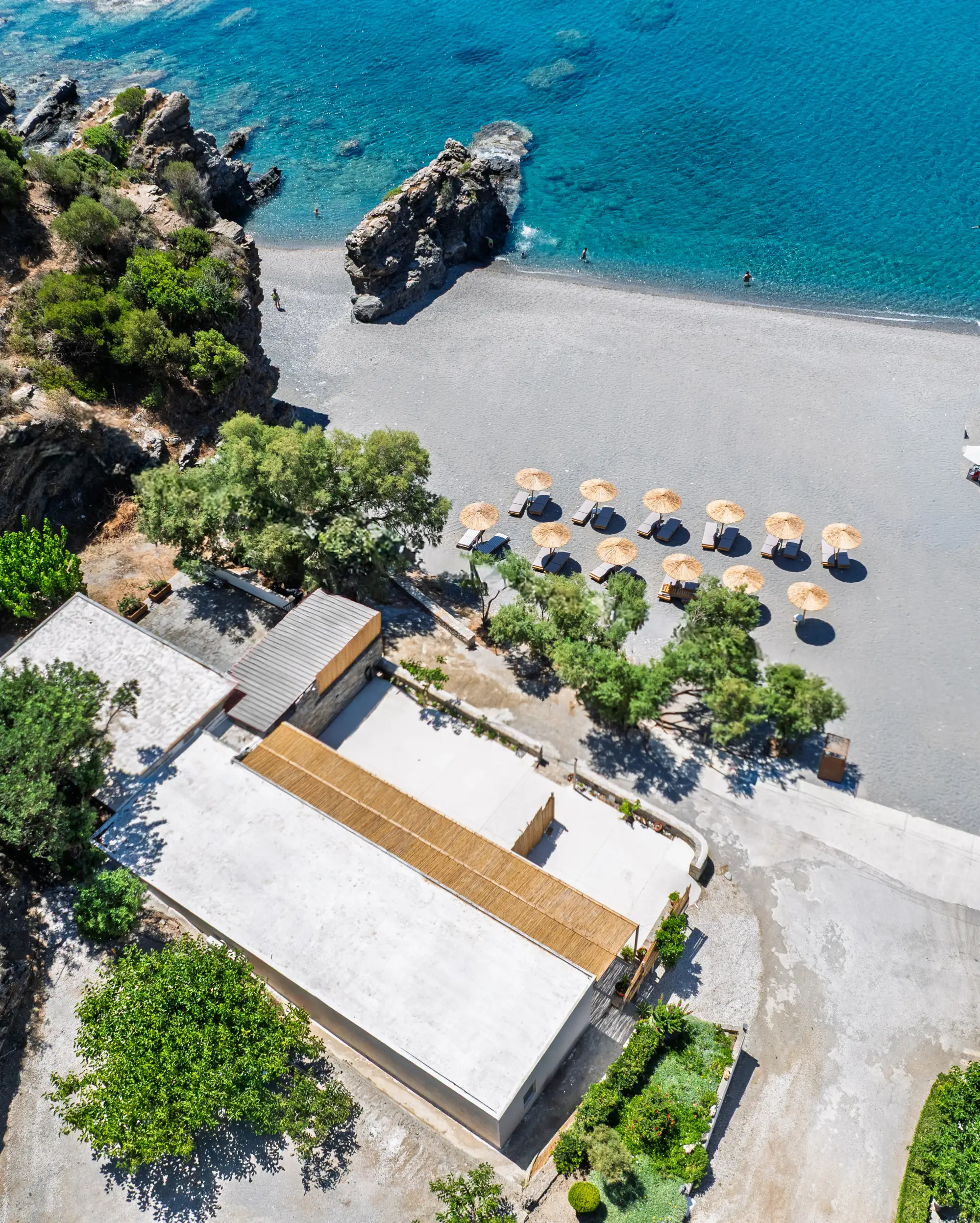 Looking down on the house roof and bamboo pergola, umbrella rows on the pebbles and the sea stack beyond