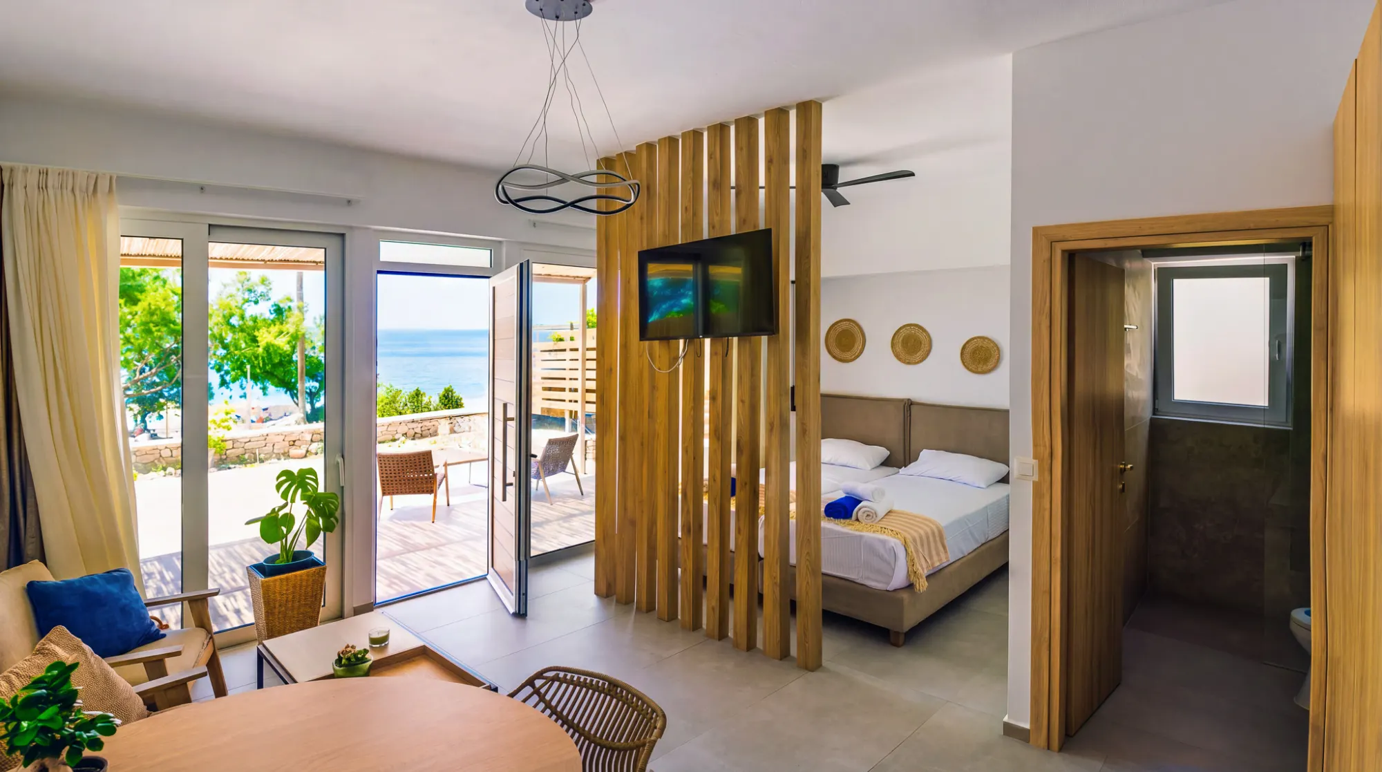 The studio's open plan — slatted oak divider between bed and sitting area, terrace door open to the sea